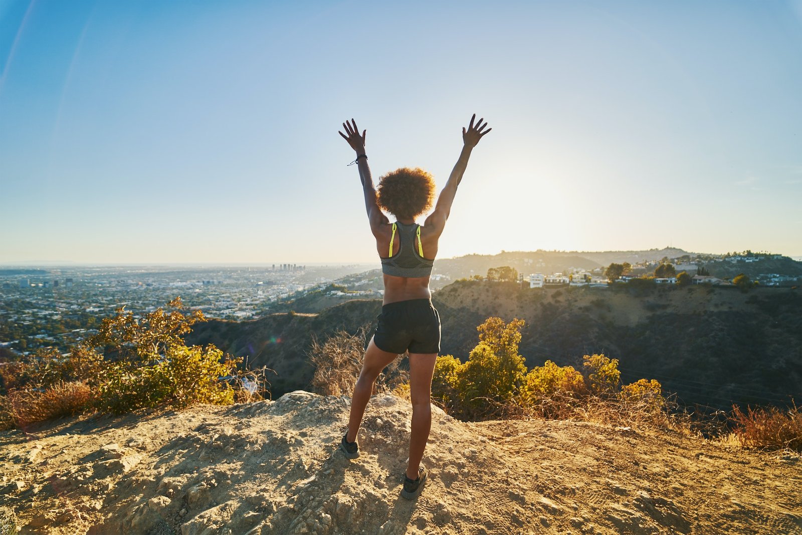 athletic african american woman celebrating reaching top of runyon canyon with arms open