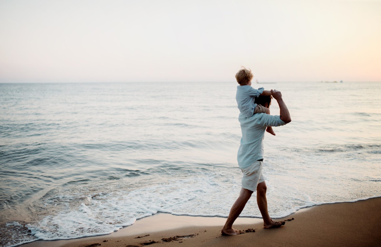 Father with a toddler boy walking on beach on summer holiday, having fun.