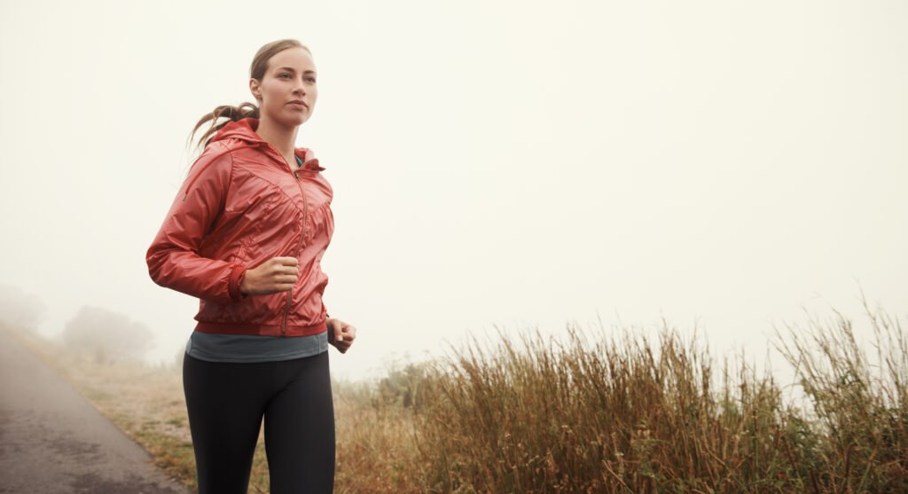 Running in solitude. A young woman running along a road on a misty morning.