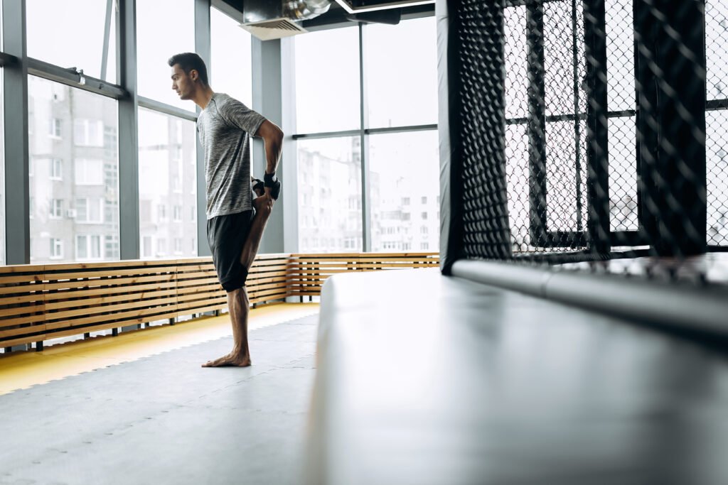 Guy dressed in the grey t-shirt stretches his arms in the boxing gym with panoramic windows